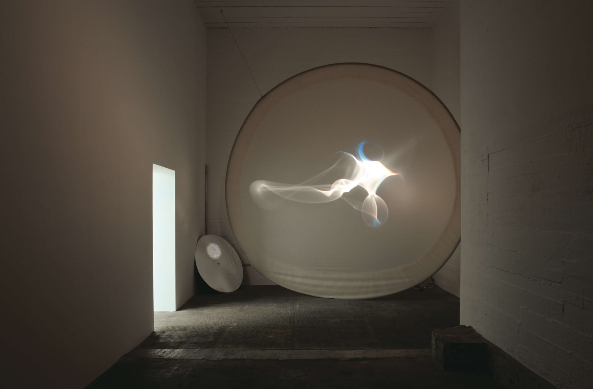 Lichtprojektion auf runder Leinwand erzeugt abstrakte, wellenförmige Reflexionen in abgedunkeltem Raum.