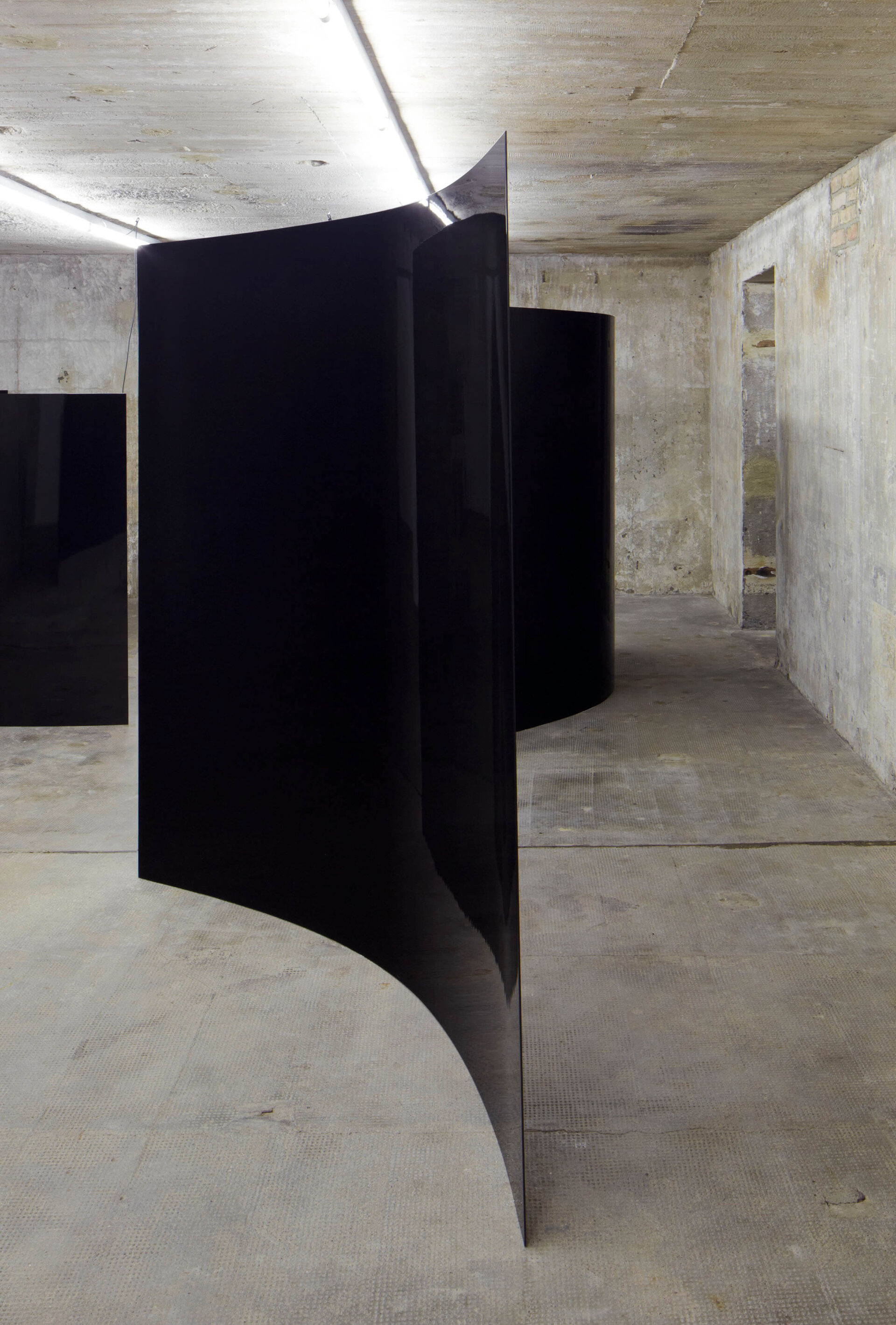 Großformatige, schwarz glänzende Flächen hängen gebogen im Raum: Alicja Kwades Installation Der Tag ohne Gestern (Dimension 1–11) von 2009, ausgestellt in einem Betonraum der Boros Collection.