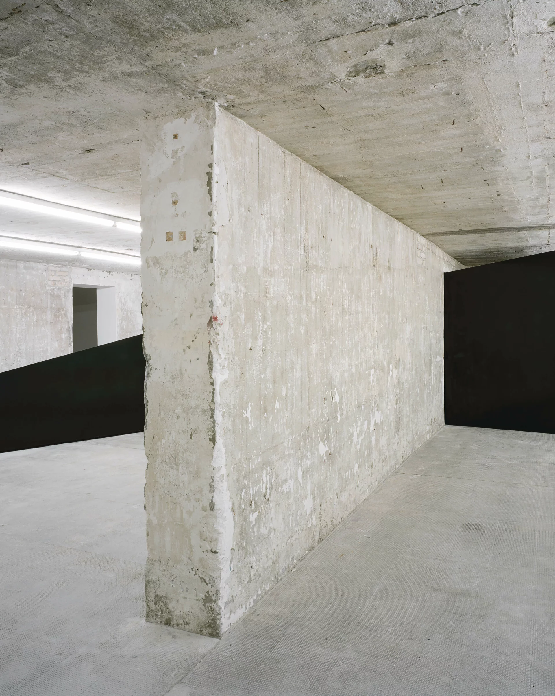 Schwarze Metallskulptur verläuft quer durch mehrere Bunkerräume, kontrastiert mit der rohen Betonarchitektur des Ausstellungsorts.