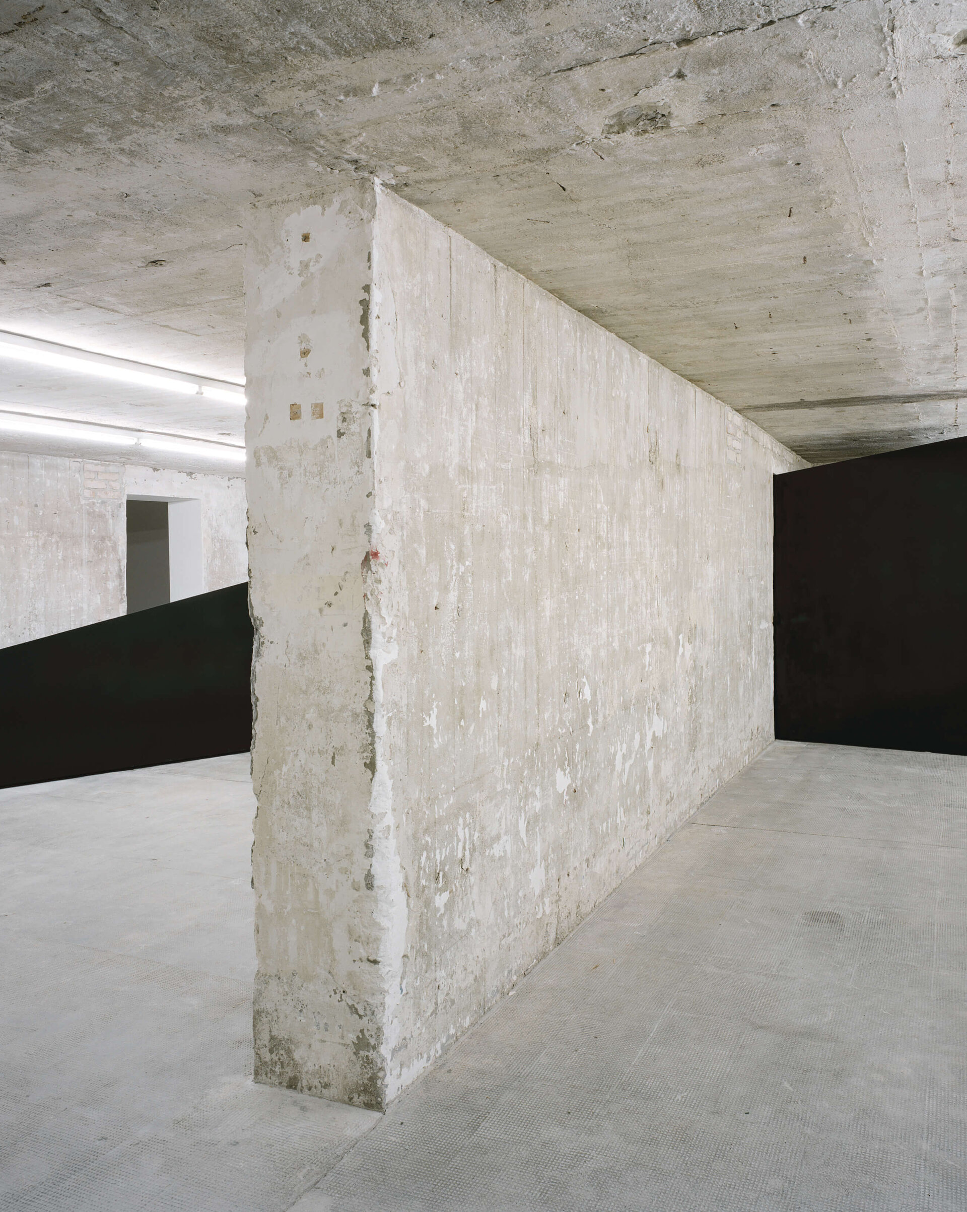Schwarze Metallskulptur verläuft quer durch mehrere Bunkerräume, kontrastiert mit der rohen Betonarchitektur des Ausstellungsorts.