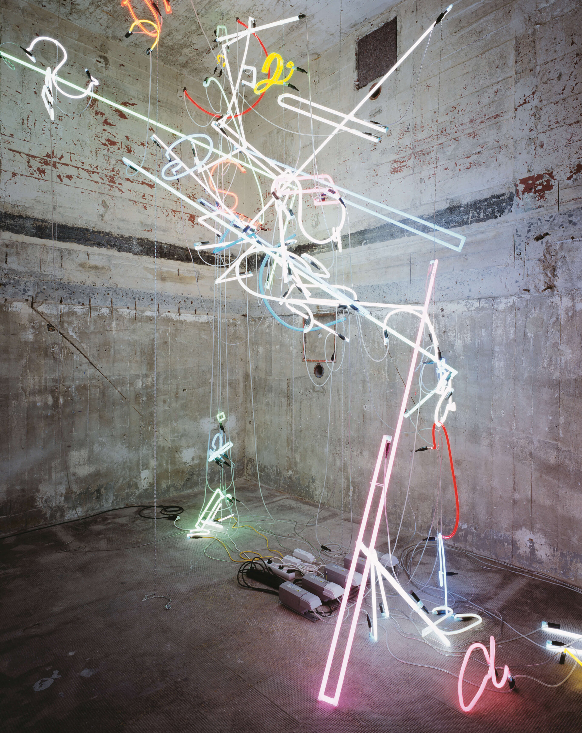 Abstrakte Neonröhren in leuchtenden Farben hängen chaotisch in einem Betonraum des Bunkers.