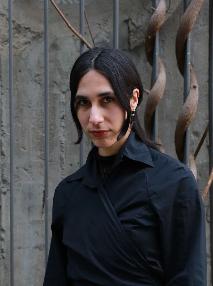 Beatriz vom Team der Boros Collection steht vor einer verwitterten Betonwand mit Rankgittern und Kletterpflanzen.