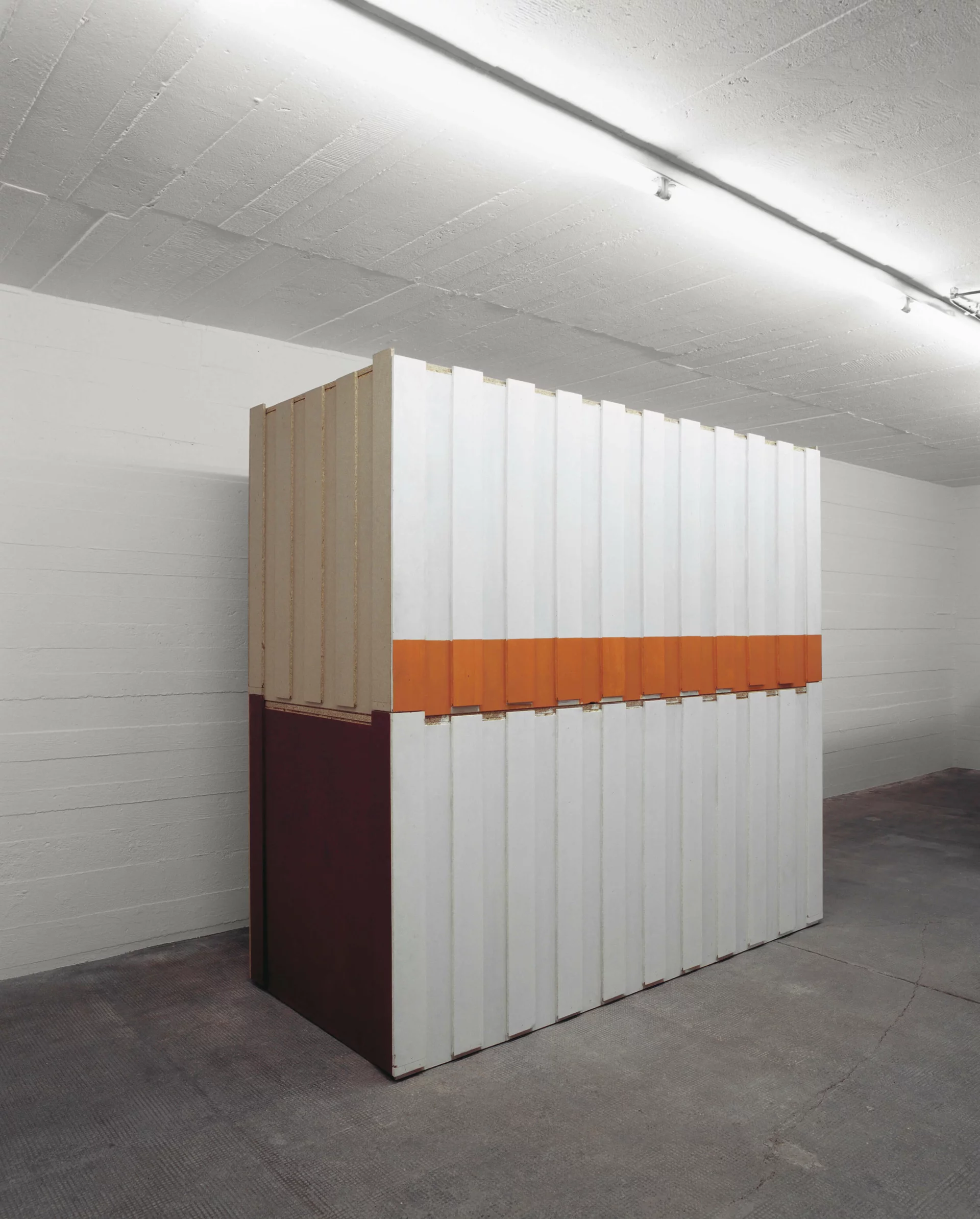 Skulptur aus vertikalen Paneelen mit weißen, orangefarbenen und weinroten Flächen in einem weißen Ausstellungsraum.