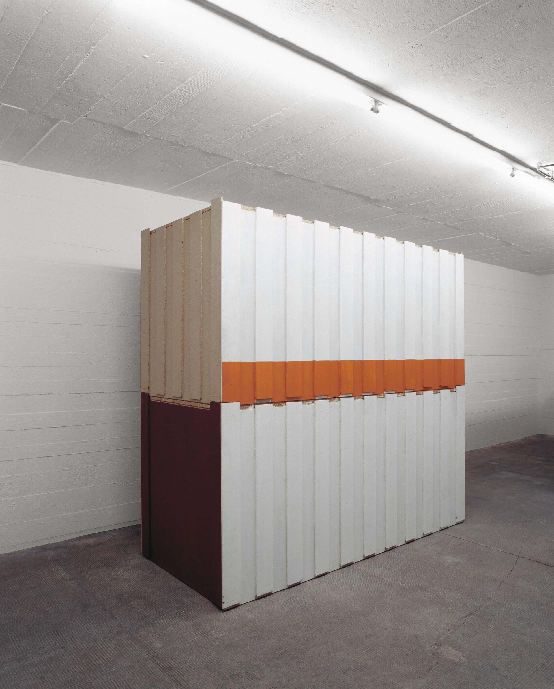 Skulptur aus vertikalen Paneelen mit weißen, orangefarbenen und weinroten Flächen in einem weißen Ausstellungsraum.