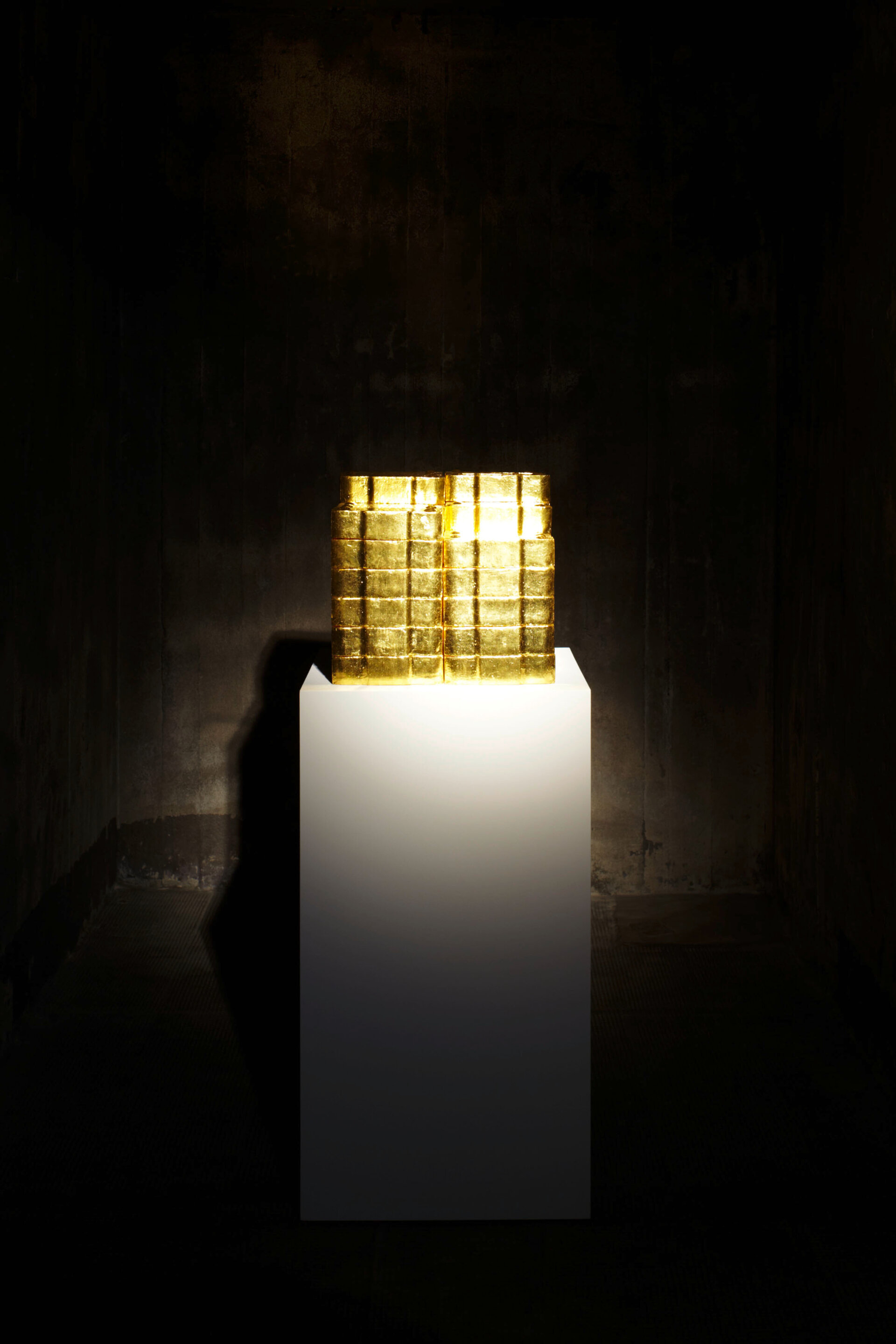 Alicja Kwades Kohle (2006): Goldüberzogene Briketts auf weißem Sockel thematisieren Wert und Wandel in einem dunklen Raum der Boros Collection.