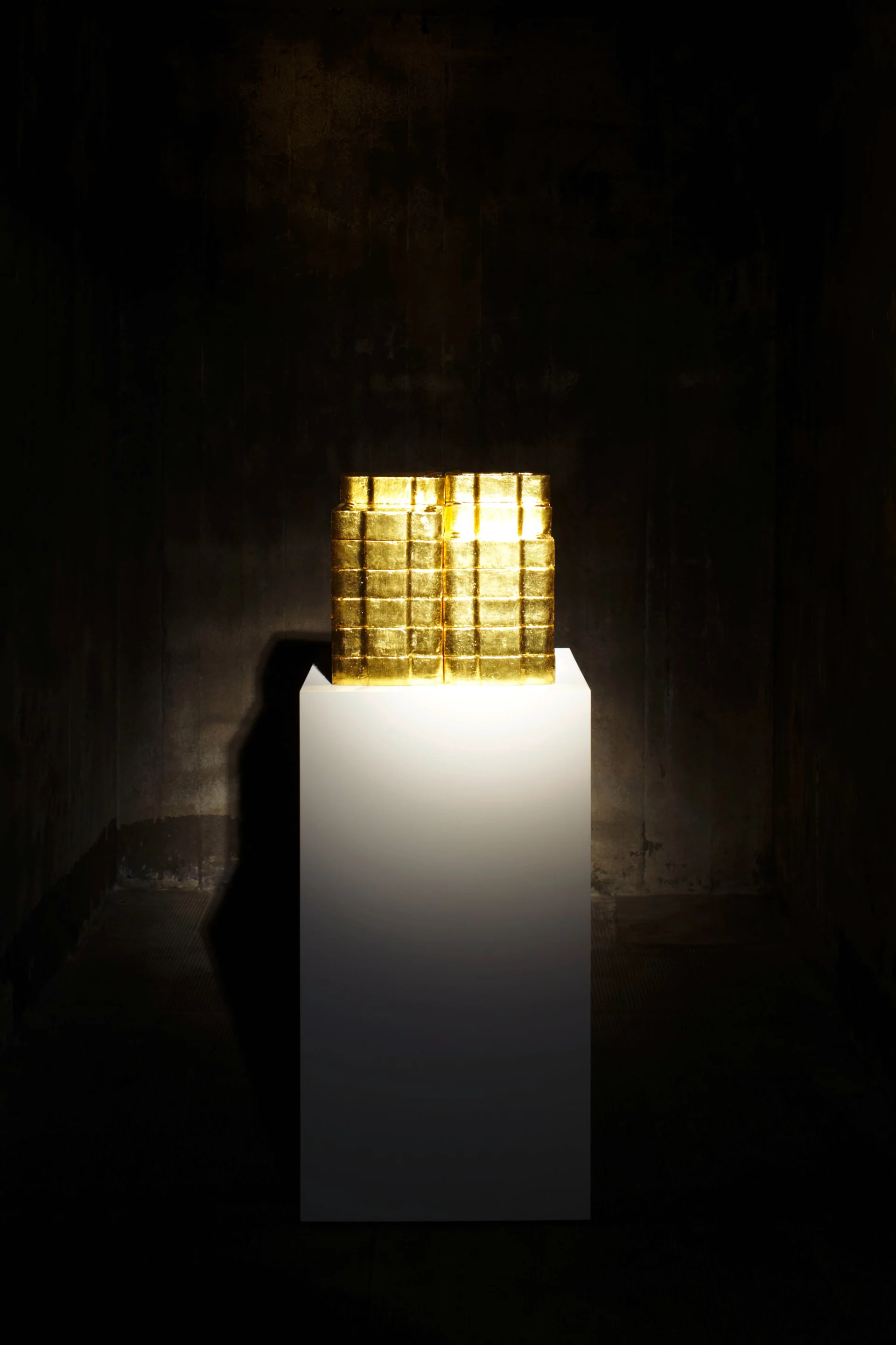 Alicja Kwades Kohle (2006): Goldüberzogene Briketts auf weißem Sockel thematisieren Wert und Wandel in einem dunklen Raum der Boros Collection.