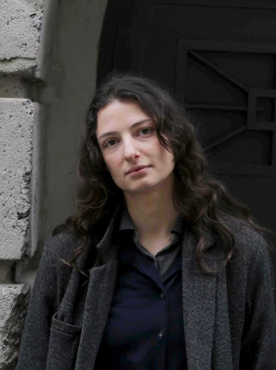 Rafaela steht im Mantel vor dem Torbogen des Bunkers – zurückhaltendes Porträt in architektonischer Umgebung.