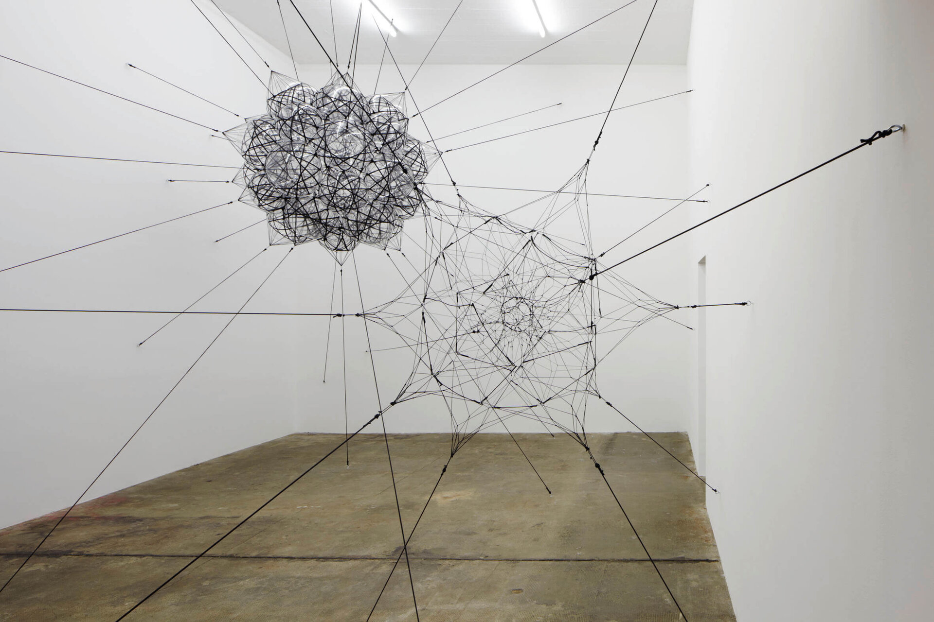 Raumfüllende Installation von Tomás Saraceno im Boros Bunker Berlin, bestehend aus schwebenden geometrischen Netzkonstruktionen aus Seilen und transparenten Materialien, die an Wänden und Decke verspannt sind.