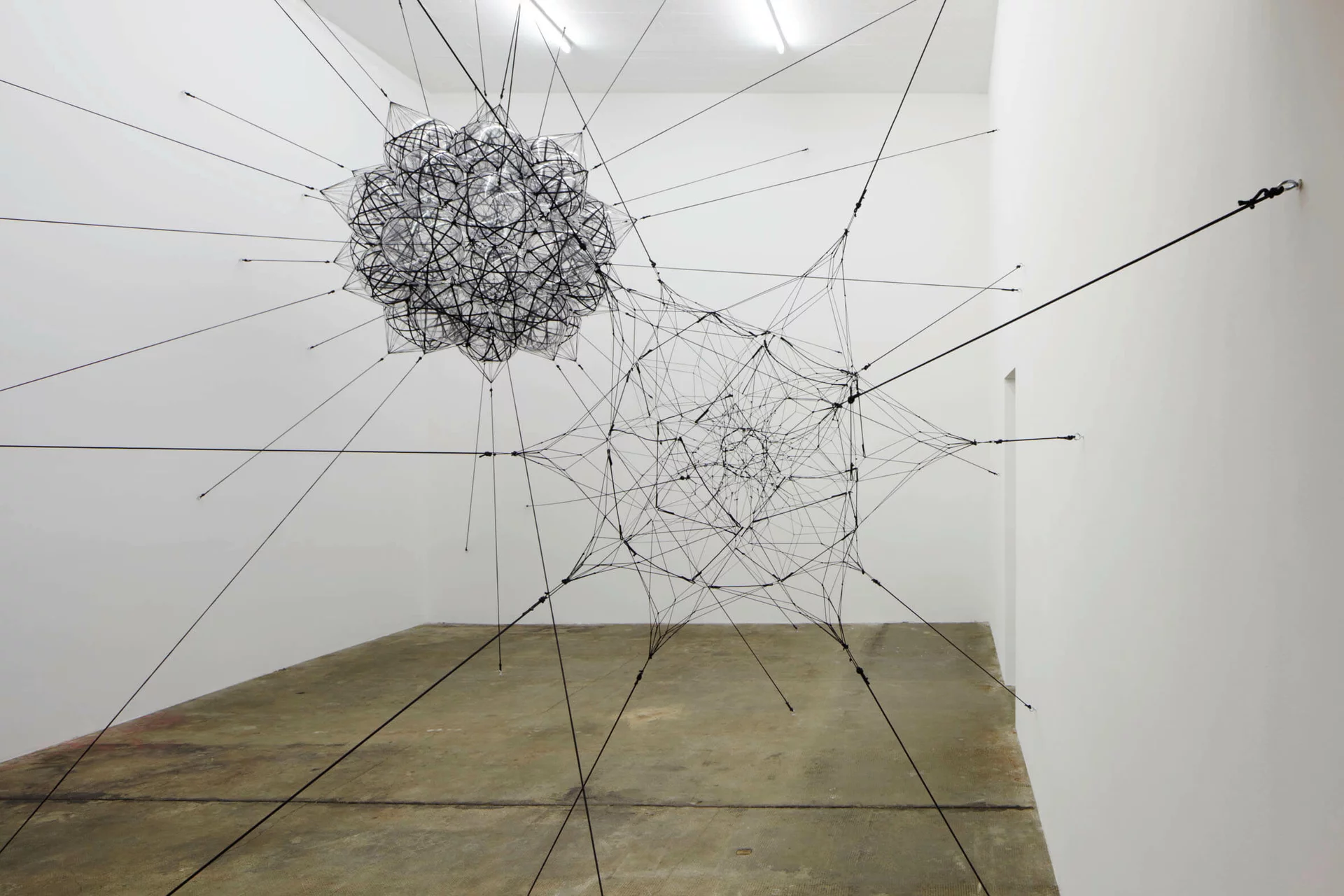 Raumfüllende Installation von Tomás Saraceno im Boros Bunker Berlin, bestehend aus schwebenden geometrischen Netzkonstruktionen aus Seilen und transparenten Materialien, die an Wänden und Decke verspannt sind.