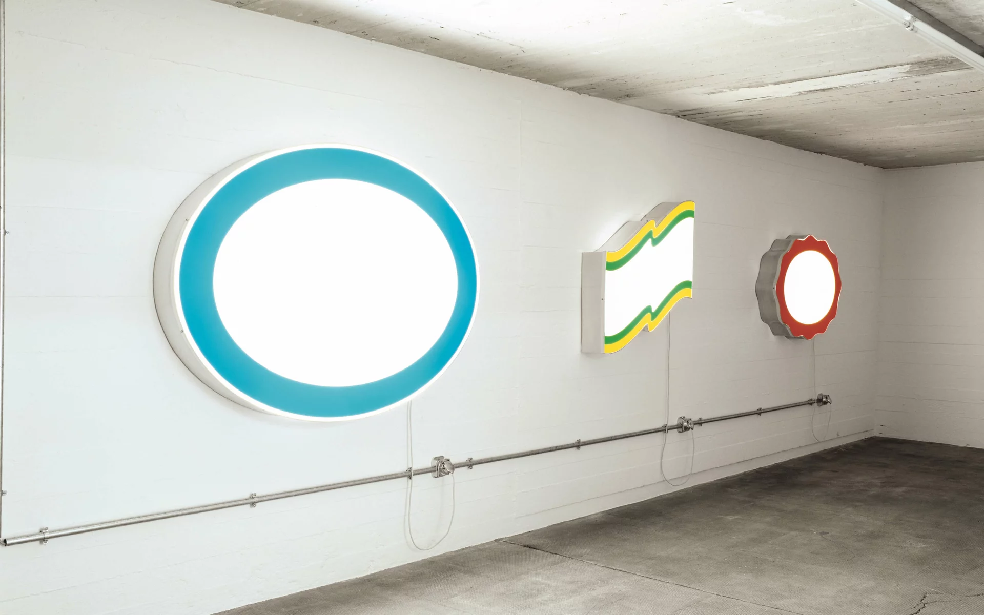 Drei leuchtende Werbesign-Objekte ohne Logos in verschiedenen Formen an einer weißen Wand.