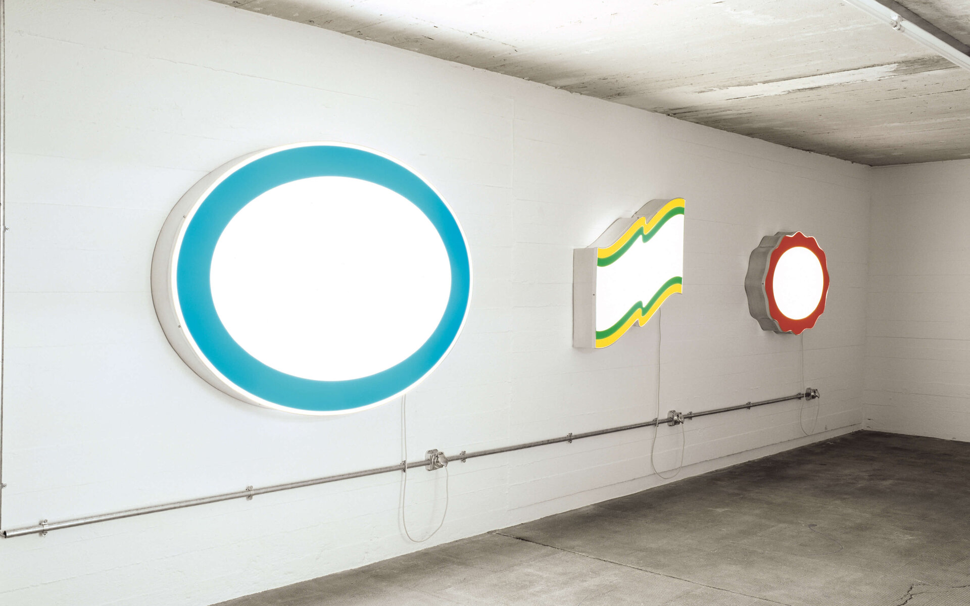 Drei leuchtende Werbesign-Objekte ohne Logos in verschiedenen Formen an einer weißen Wand.
