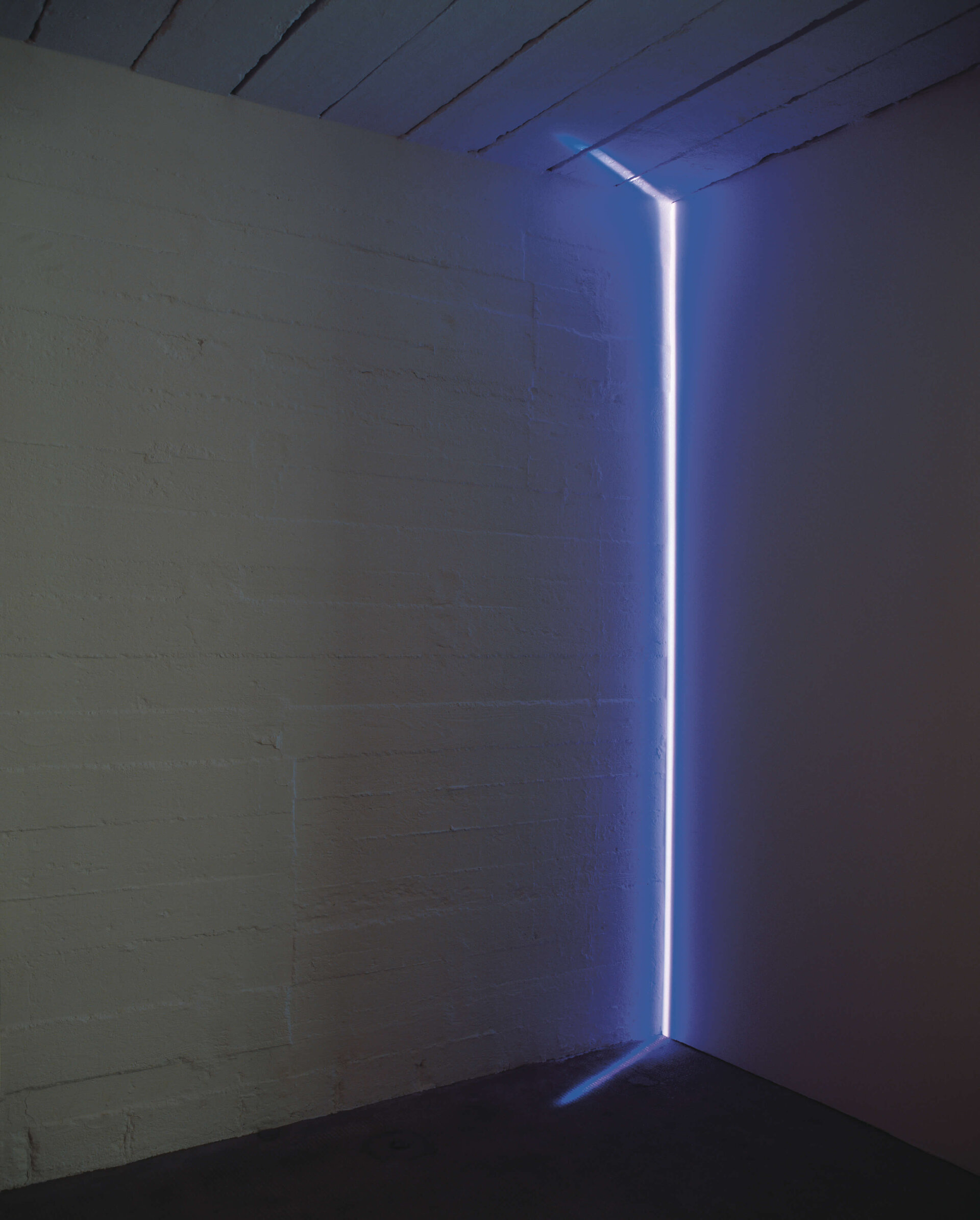 Vertikaler Lichtstrahl in kühlem Blau beleuchtet die Ecke eines dunklen Raumes und erzeugt eine klare geometrische Lichtkante.