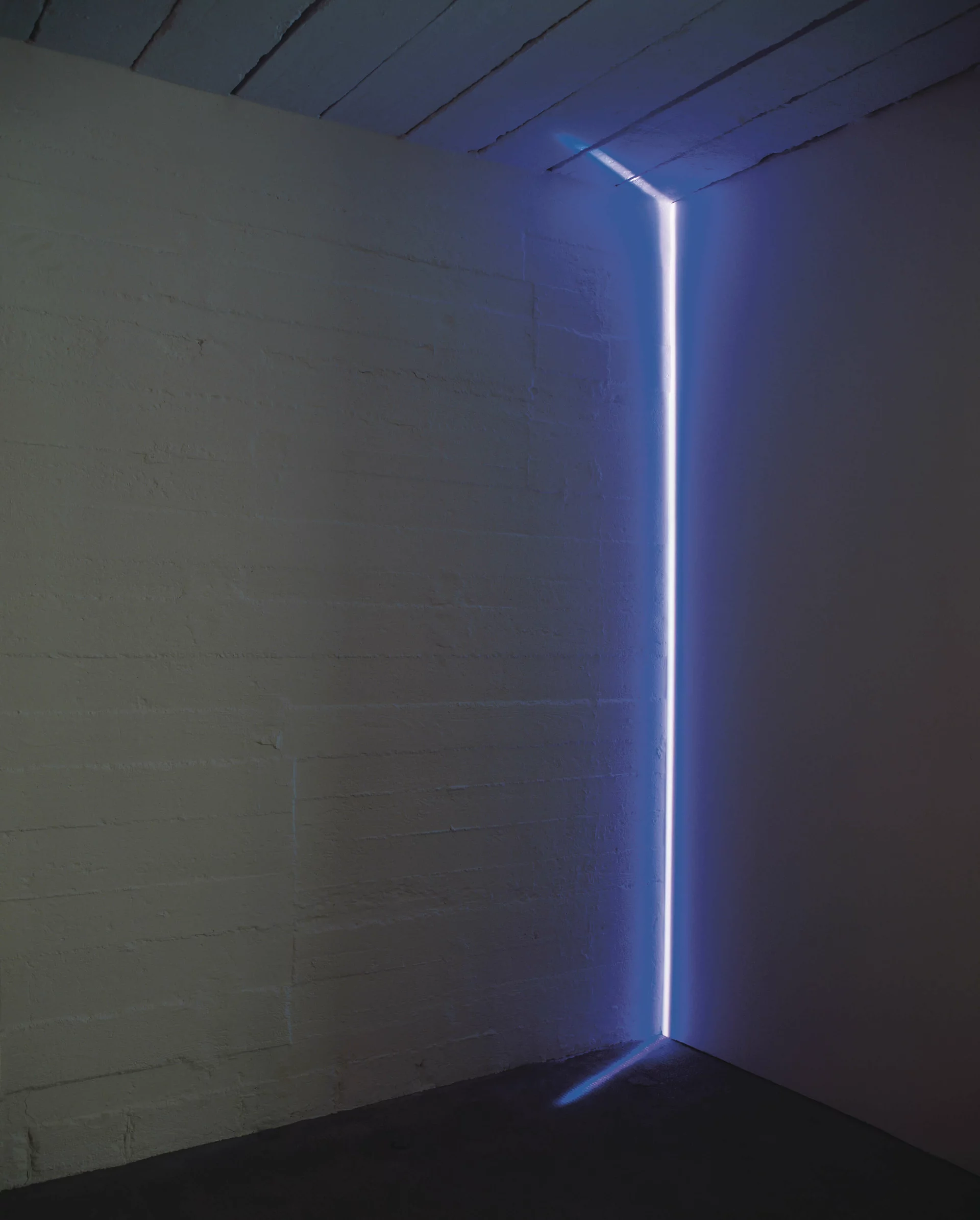 Vertikaler Lichtstrahl in kühlem Blau beleuchtet die Ecke eines dunklen Raumes und erzeugt eine klare geometrische Lichtkante.