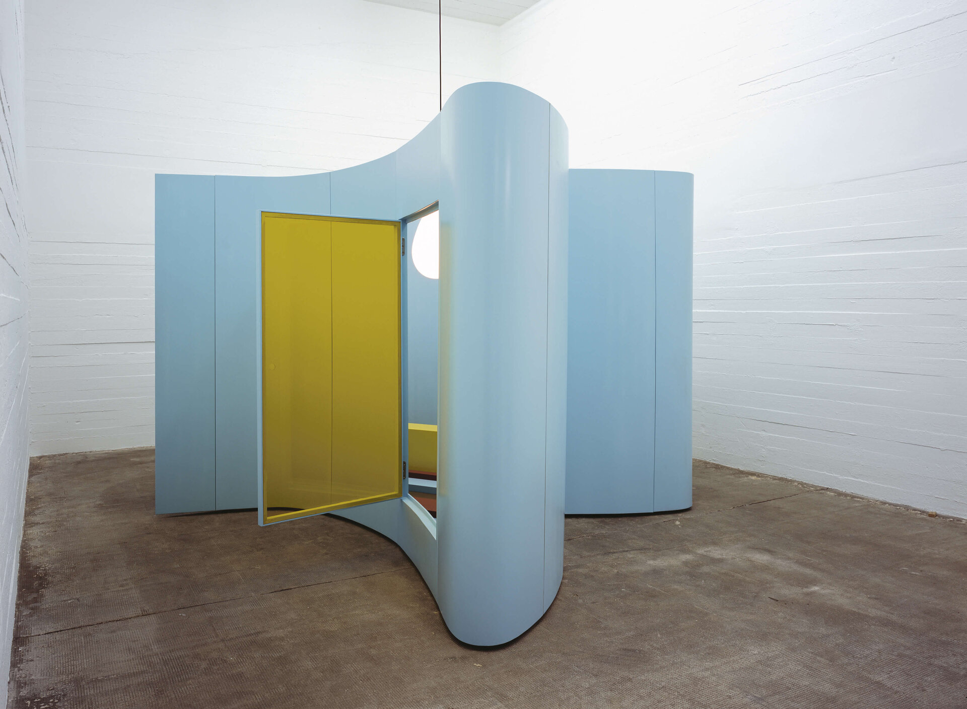 Geschwungene, pastellblaue Raumskulptur mit geöffnetem gelben Türelement in weißem Ausstellungsraum.