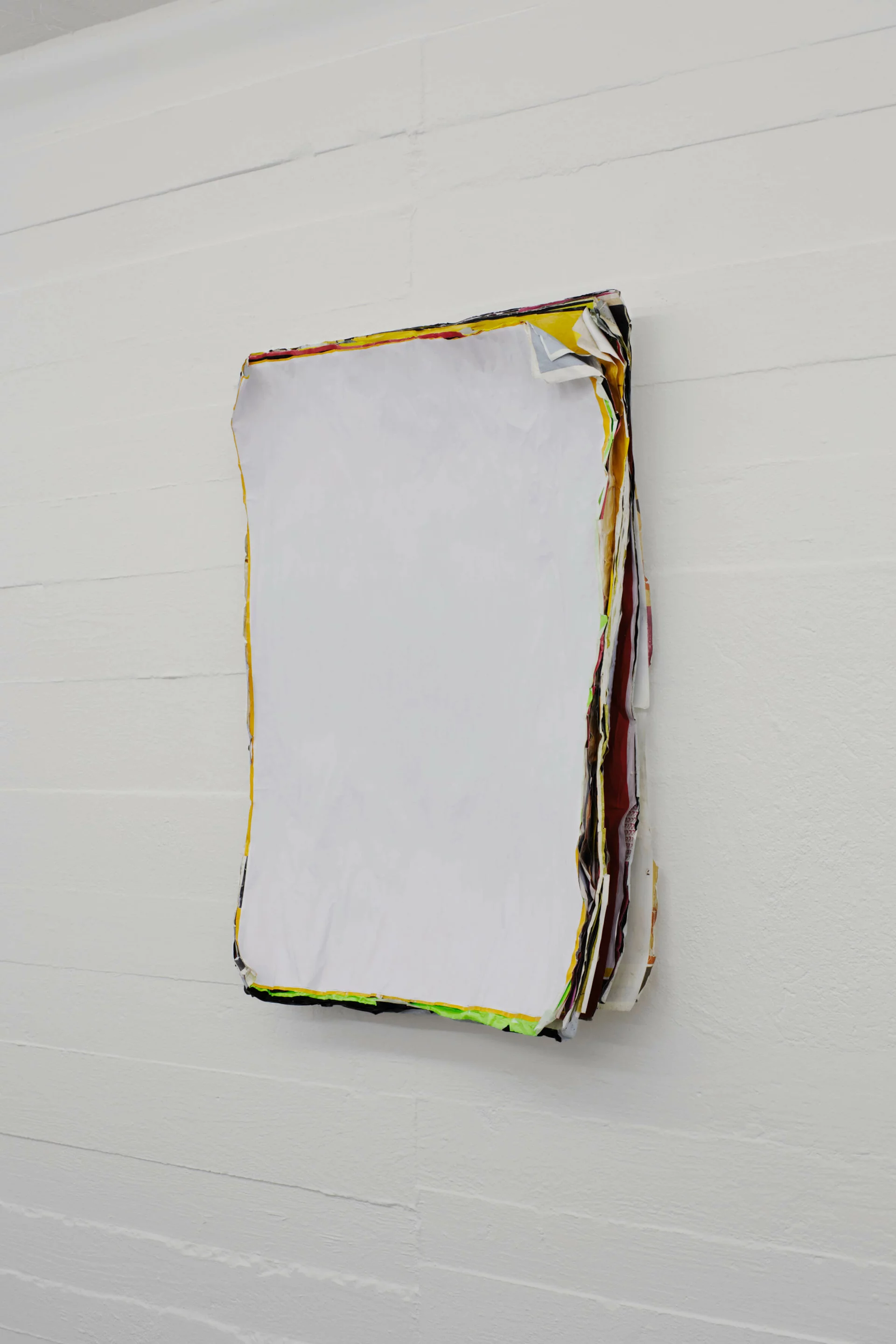 Wandobjekt von Klara Lidén bestehend aus übereinander geschichteten, teils eingerissenen und übermalten Plakaten mit weißer Fläche; die bunten Ränder deuten auf das verborgene Bildmaterial im Inneren.
