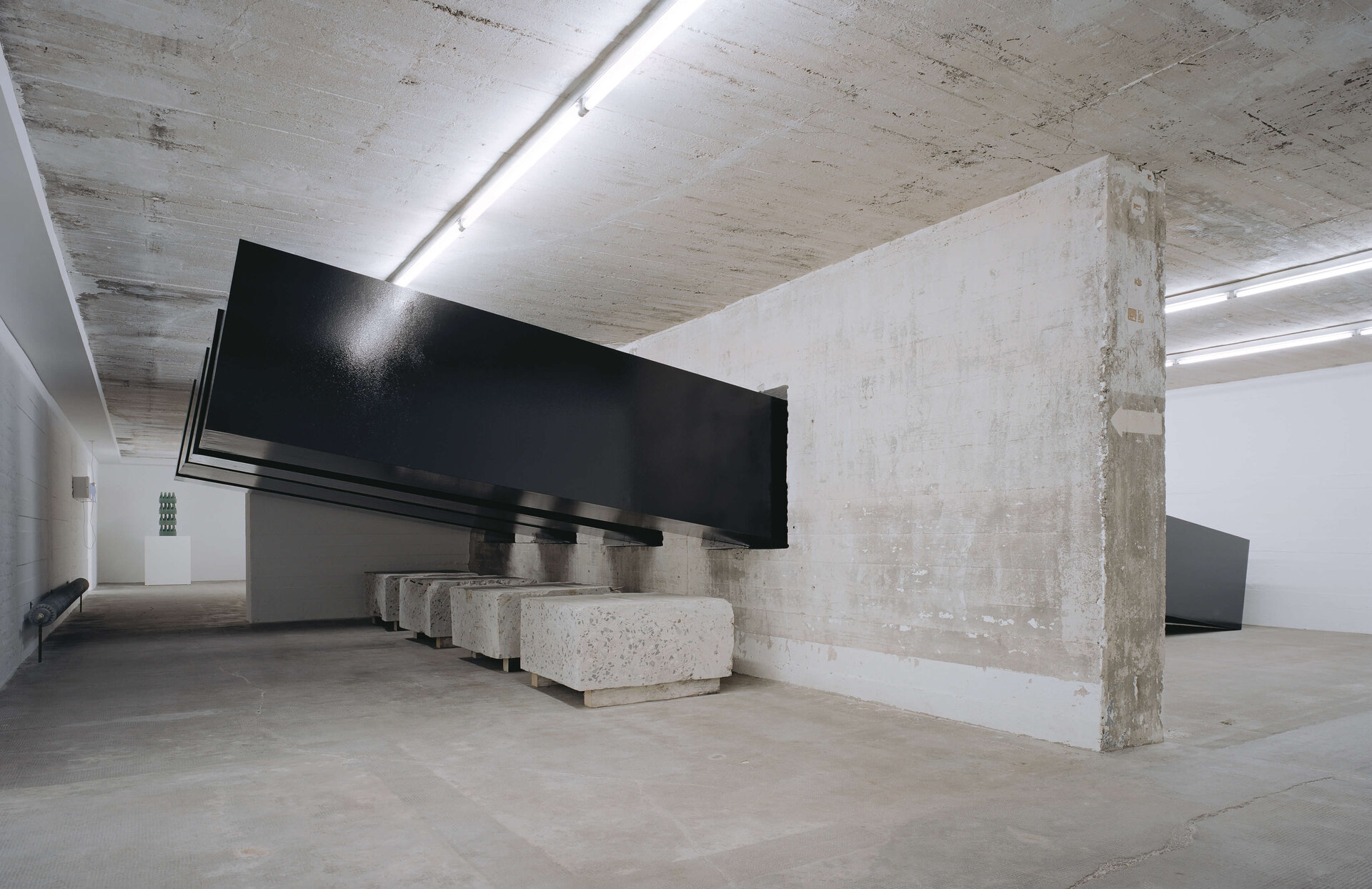 Schwarze, teerbeschichtete Balken durchdringen Wände im Bunkerraum; massives, geometrisches Kunstwerk im Kontrast zur Betonarchitektur.