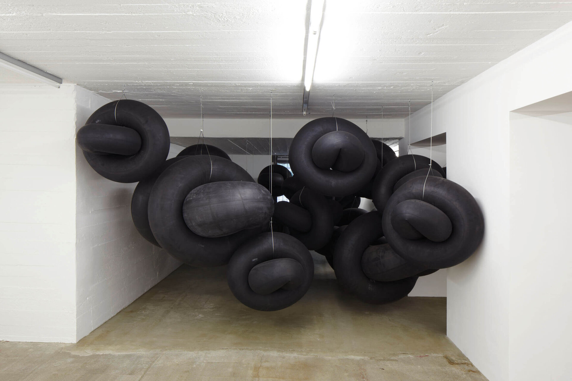 Schwarze Gummischläuche hängen geknotet von der Decke in einem weißen Raum im Boros Bunker Berlin.