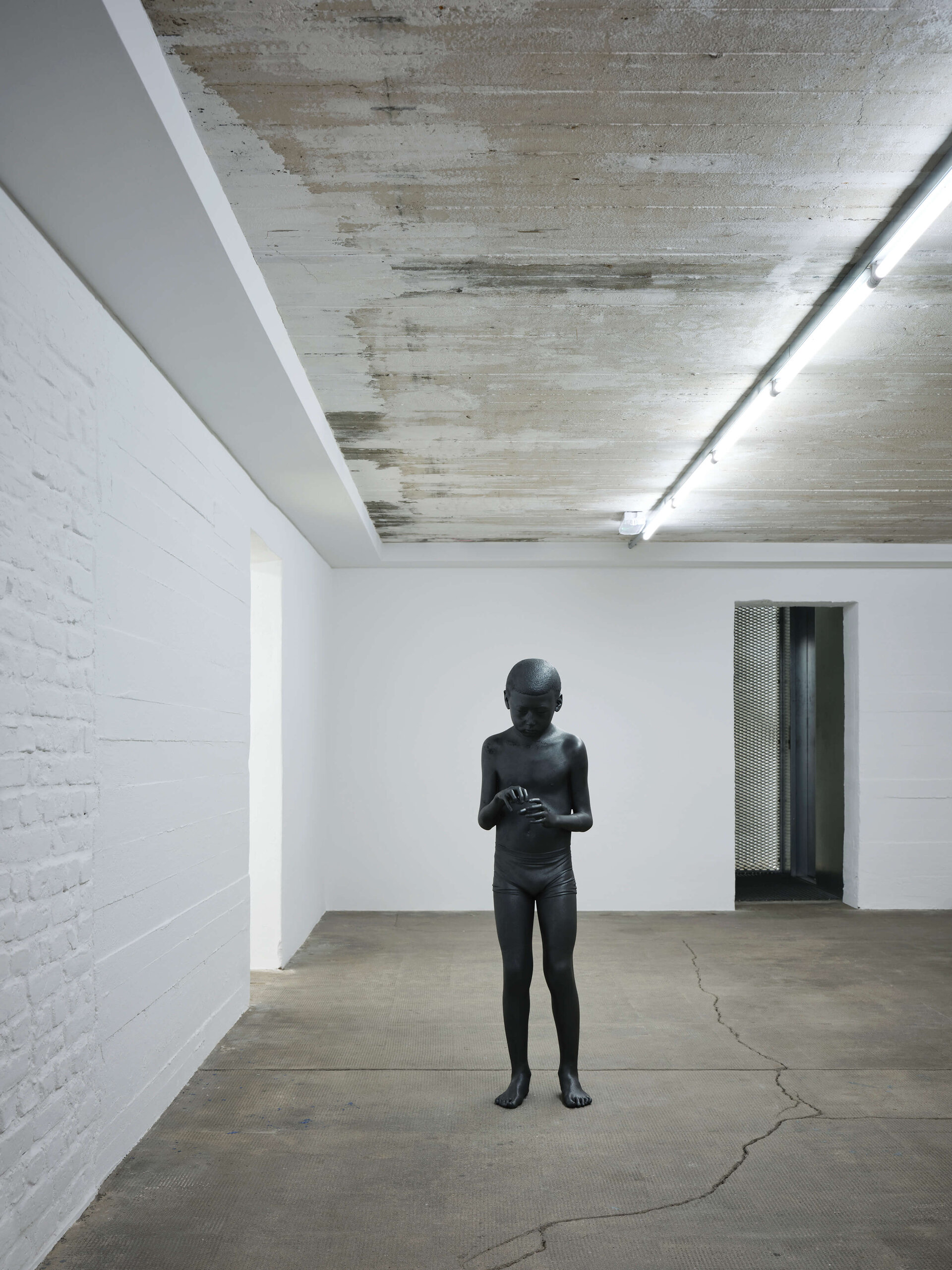 Schwarze Skulptur eines Jungen steht in einem weißen Ausstellungsraum der Boros Collection
