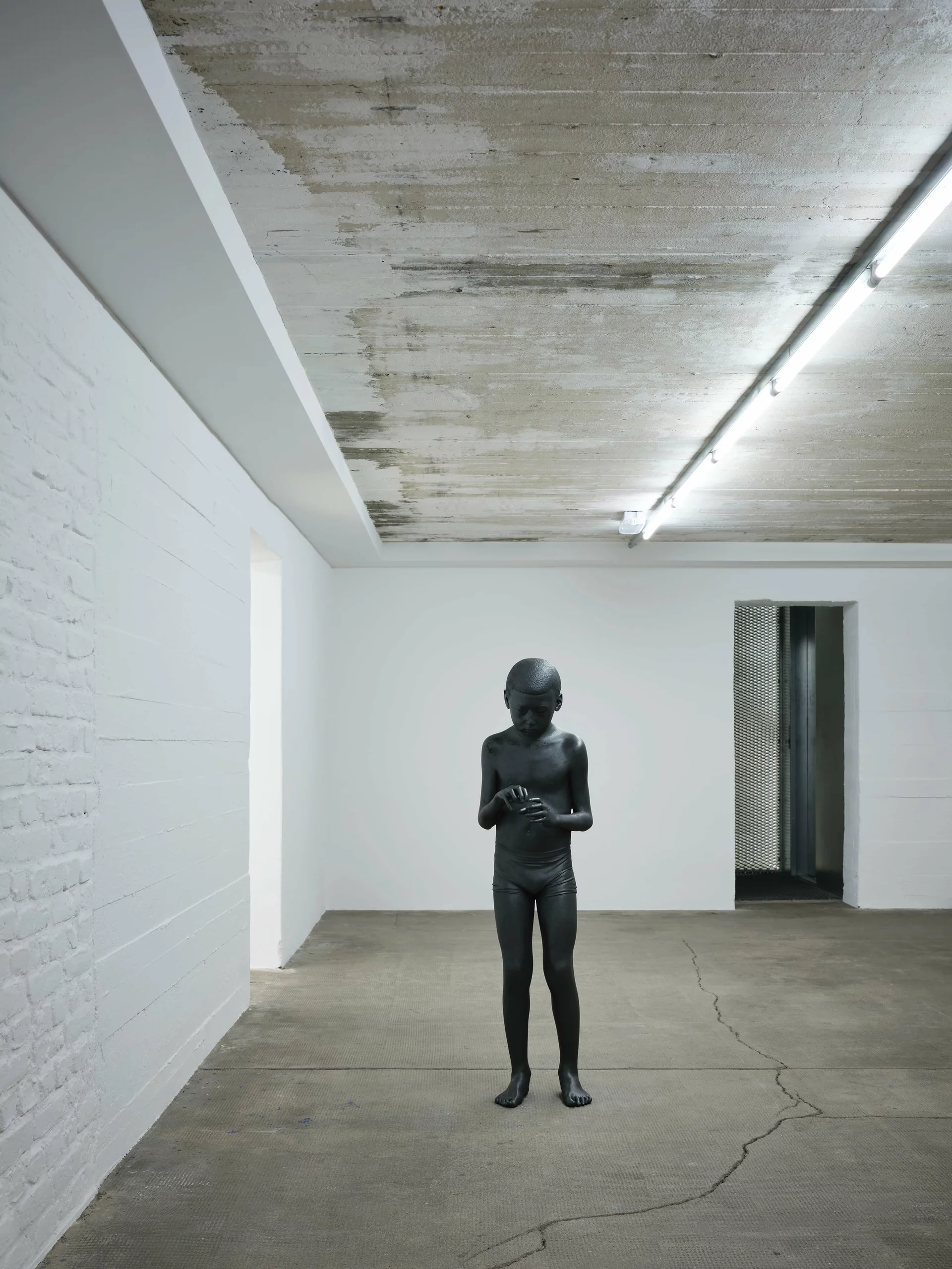 Schwarze Skulptur eines Jungen steht in einem weißen Ausstellungsraum der Boros Collection