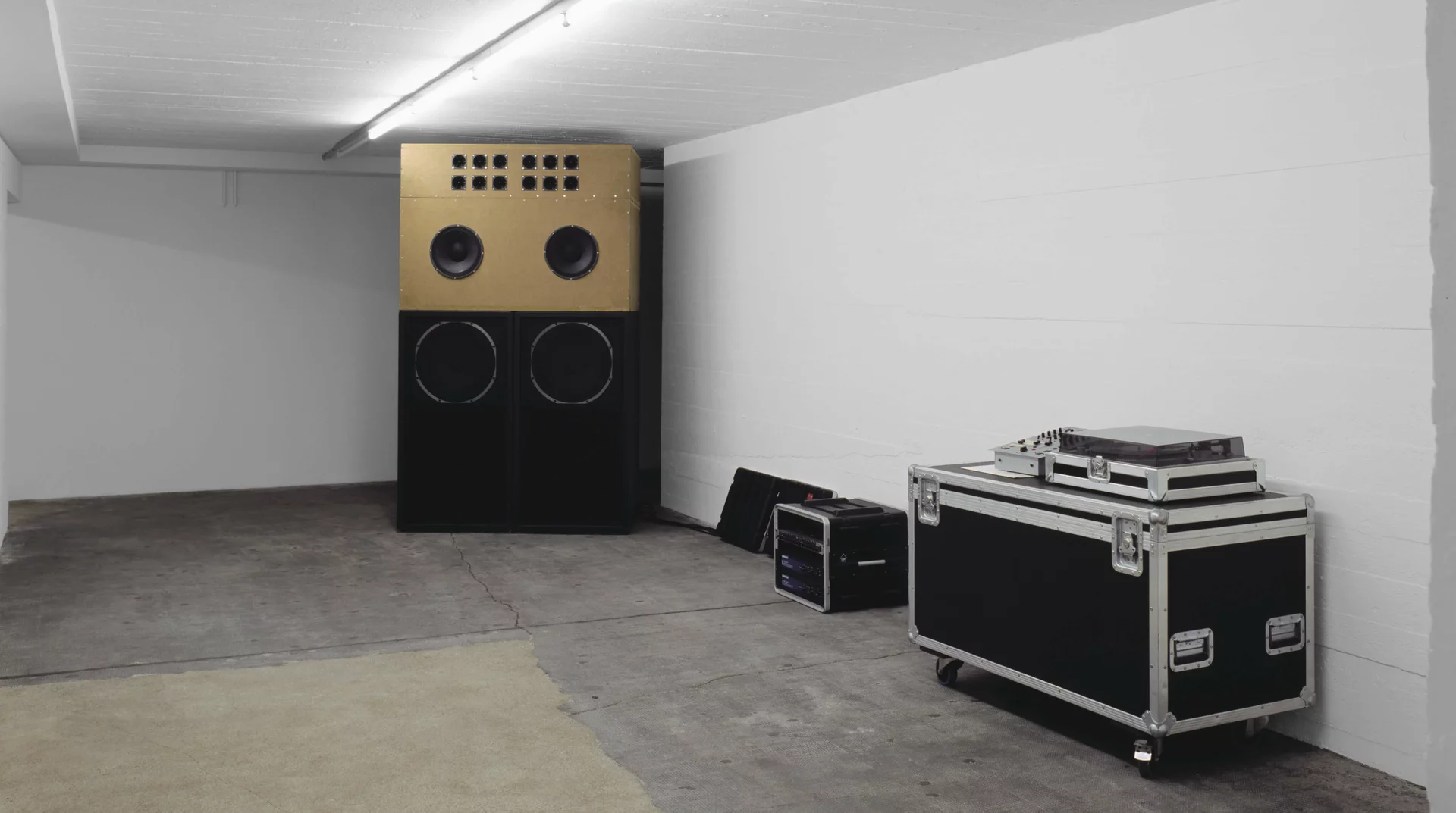 Installation mit gold-schwarzer Soundanlage, DJ-Equipment und Flightcase in weißem Ausstellungsraum.