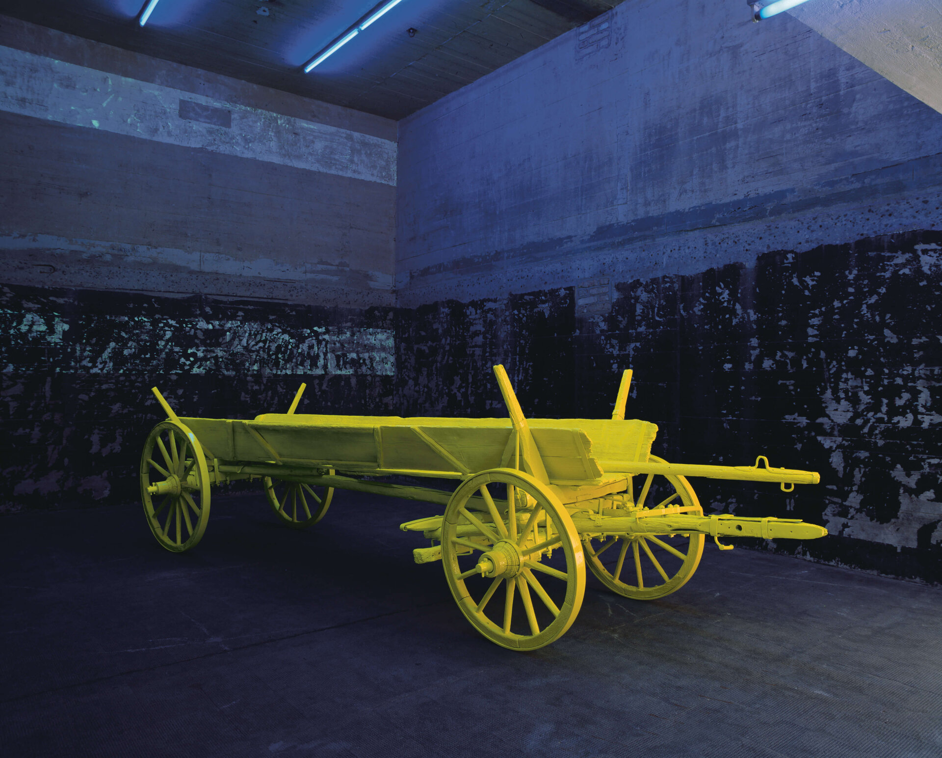 Grellgelber Holzwagen in dunklem Raum, inszeniert unter blauem Schwarzlicht.