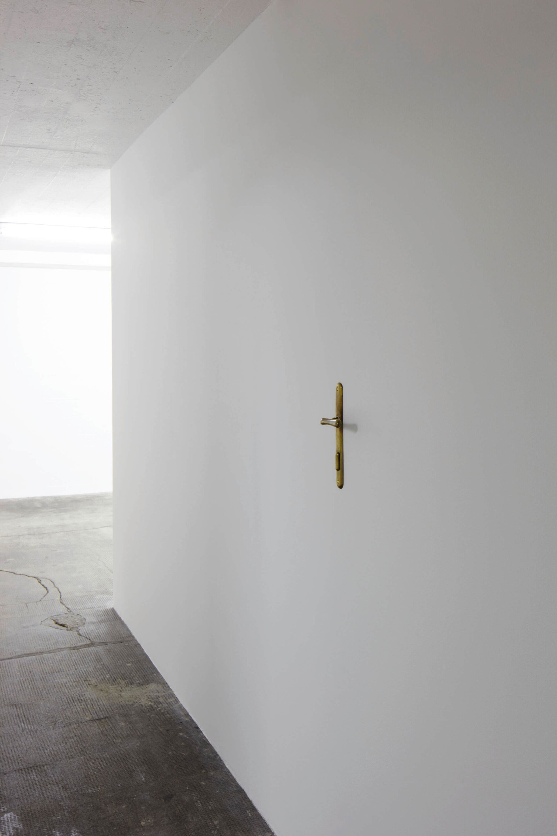 Vergoldete Türklinke ohne Tür, direkt in eine weiße Wand montiert im Boros Bunker Berlin