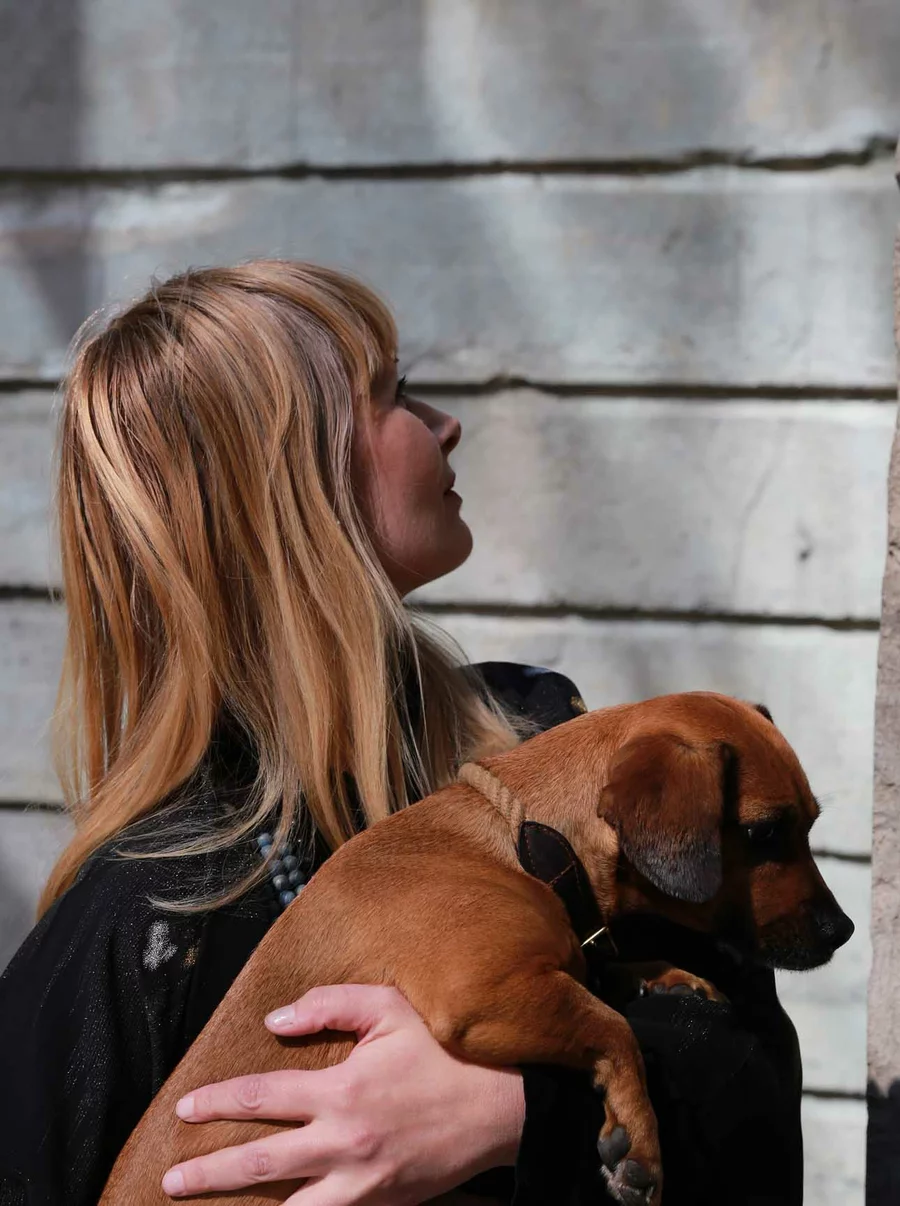 Wencke im Profil, hält einen kleinen braunen Hund im Arm, Licht und Schatten auf der Betonwand im Hintergrund.
