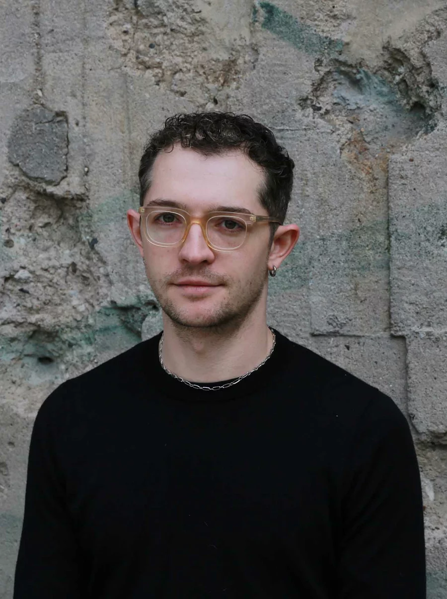 Nils in schwarzem Pullover vor der markanten, beschädigten Betonwand des Bunkers, Teil des Teams der Boros Collection