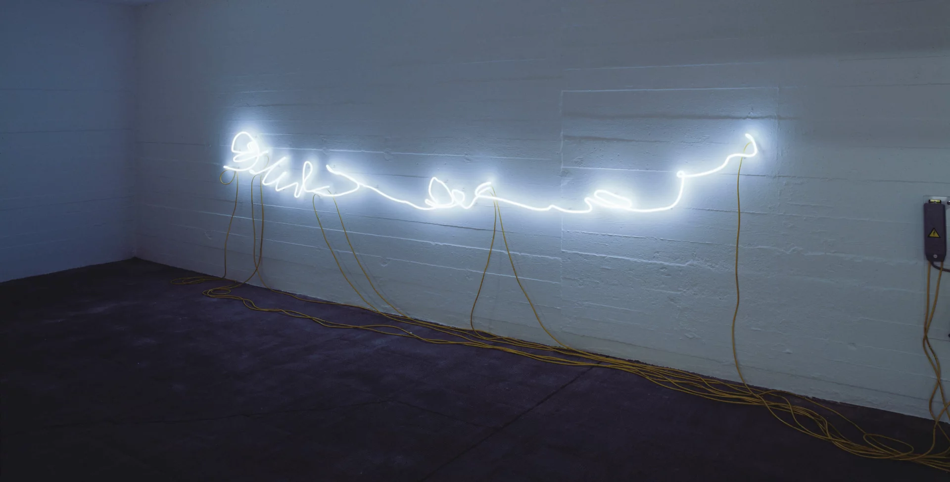 Weiße Neonlinie in Handschriftform leuchtet an einer Wand mit gelben Kabeln; Werk von Rirkrit Tiravanija.