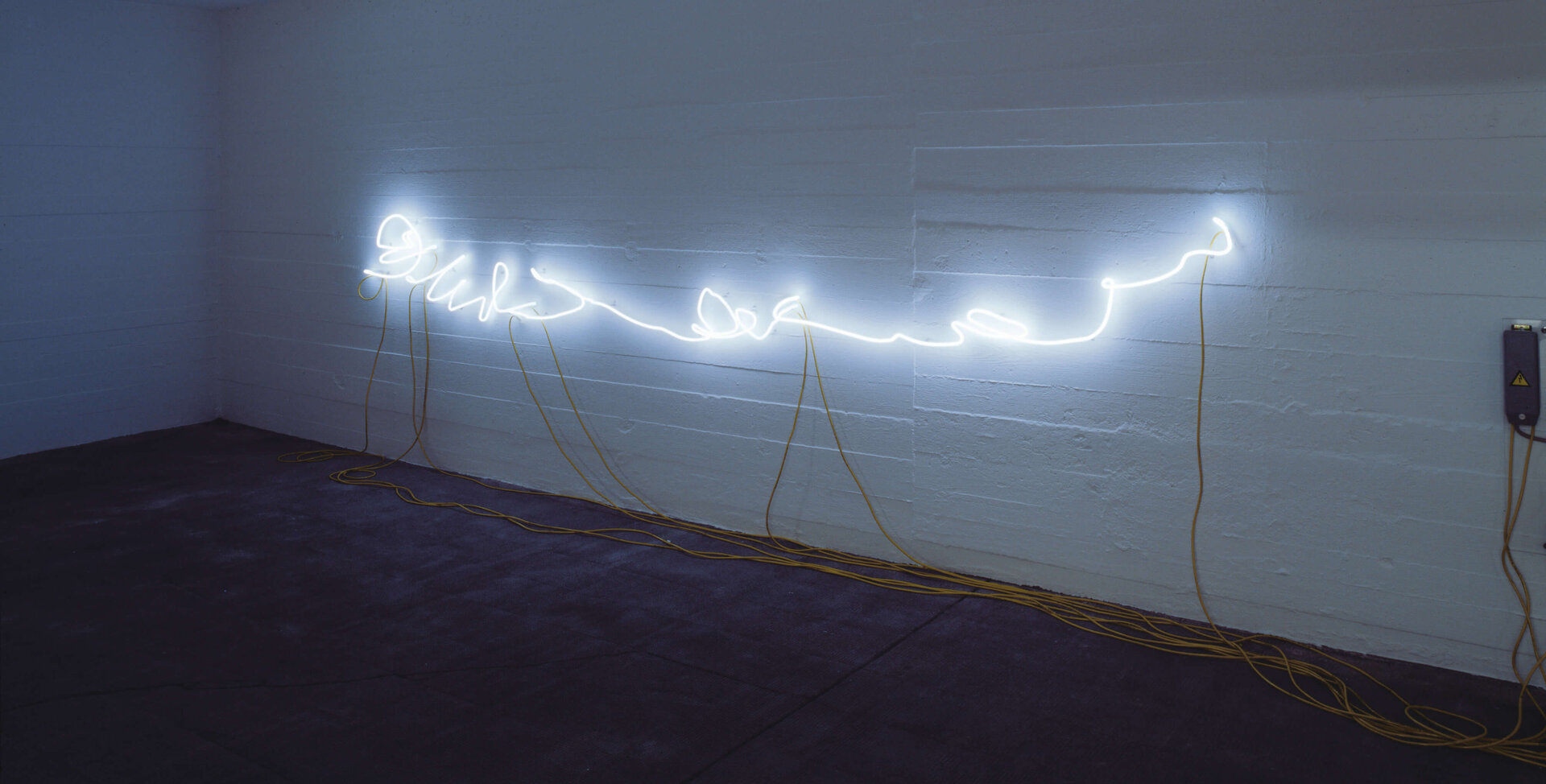 Weiße Neonlinie in Handschriftform leuchtet an einer Wand mit gelben Kabeln; Werk von Rirkrit Tiravanija.