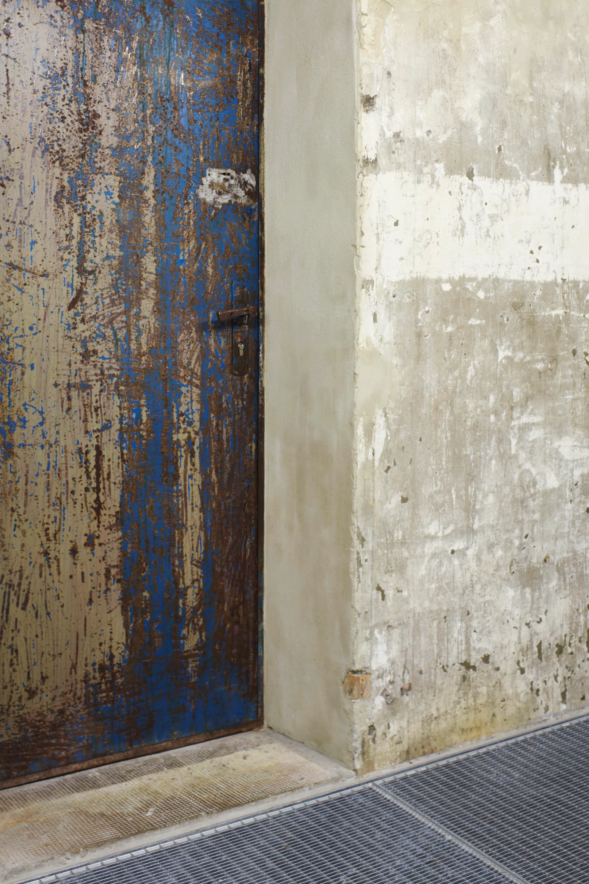 Nahaufnahme einer alten Metalltür mit abgeblätterter blauer Farbe und rostigen Stellen, daneben eine roh verputzte Wand. Das Foto zeigt ein architektonisches Detail aus dem historischen Bunker der Boros Collection in Berlin.