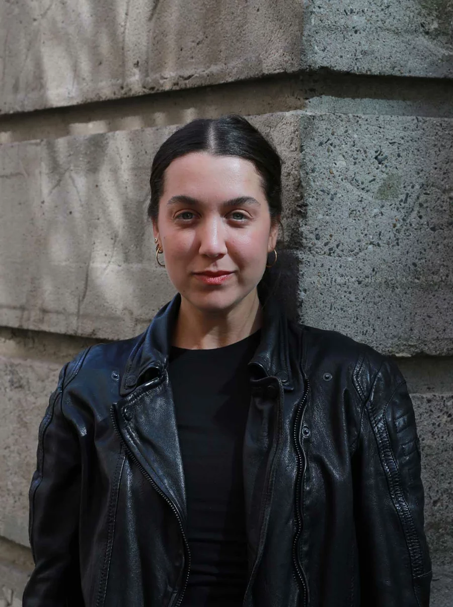 Naama steht in schwarzer Lederjacke an der Bunkerecke, Licht wirft Muster auf die Wand, Teammitglied der Boros Collection