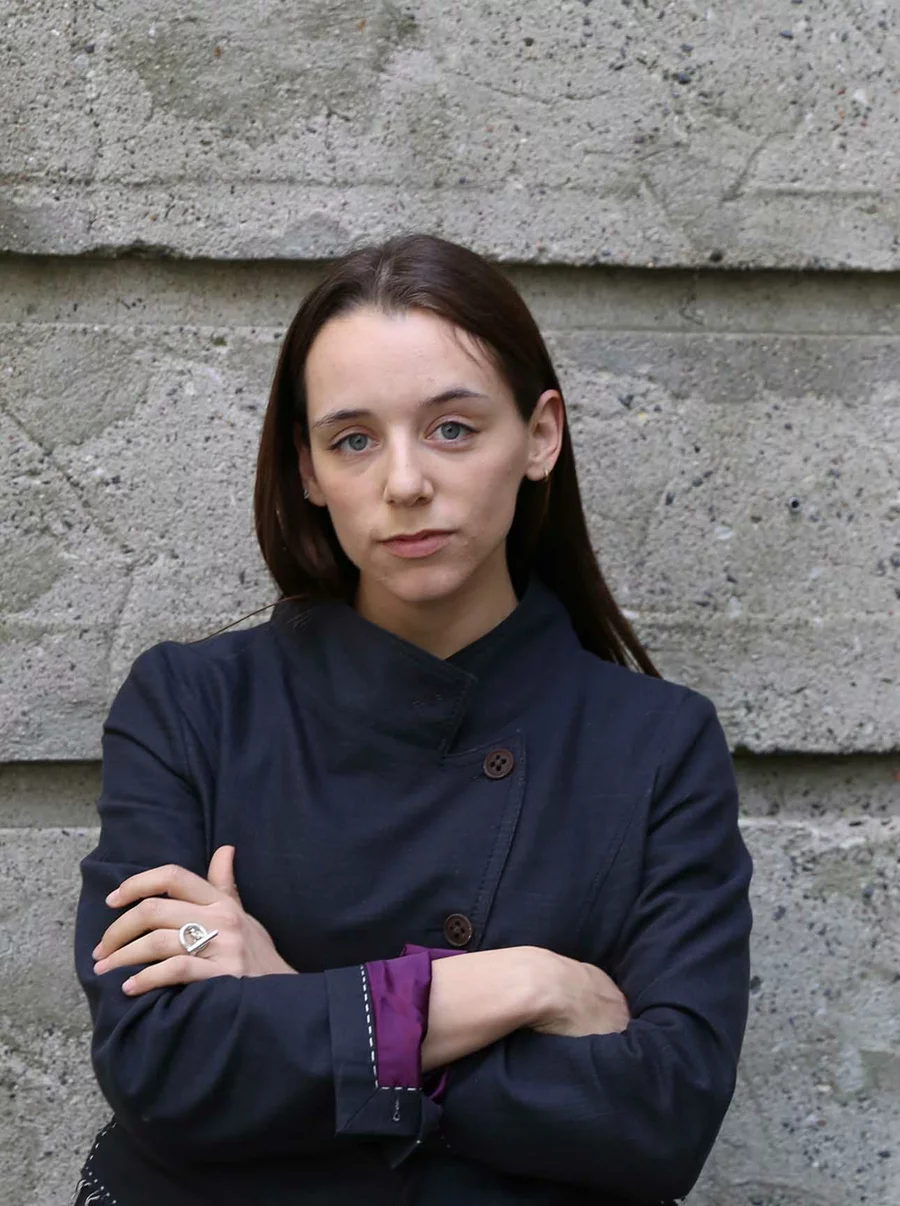 Lucie lehnt mit verschränkten Armen an der markanten Betonfassade des Boros Bunkers in Berlin