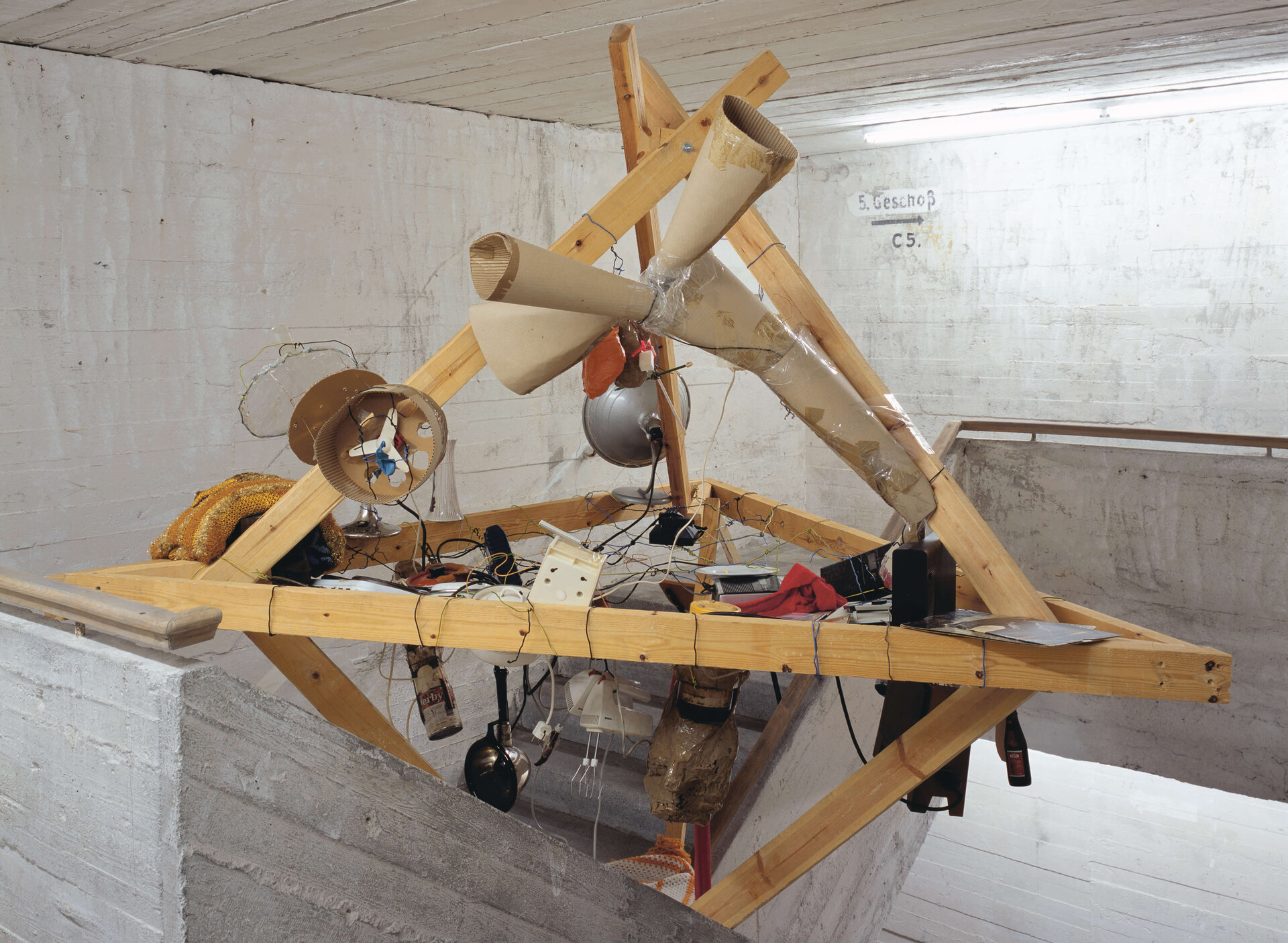 Raumgreifende Installation aus Holz, Alltagsobjekten und Kabeln, schwebend in einem Treppenhaus der Boros Collection.