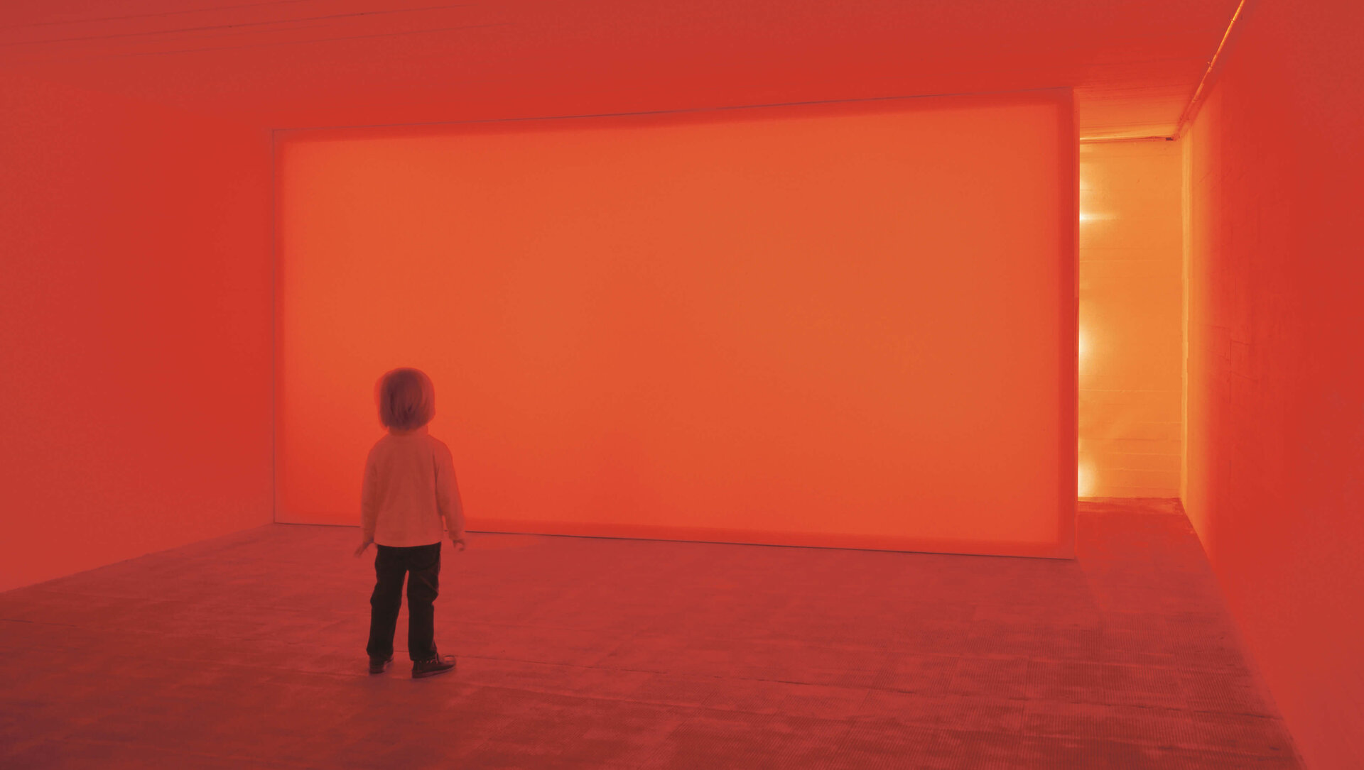 Kind steht in einem Raum, der vollständig in rotes Licht getaucht ist; Lichtfeld auf der Wand erzeugt immersive Farberfahrung.