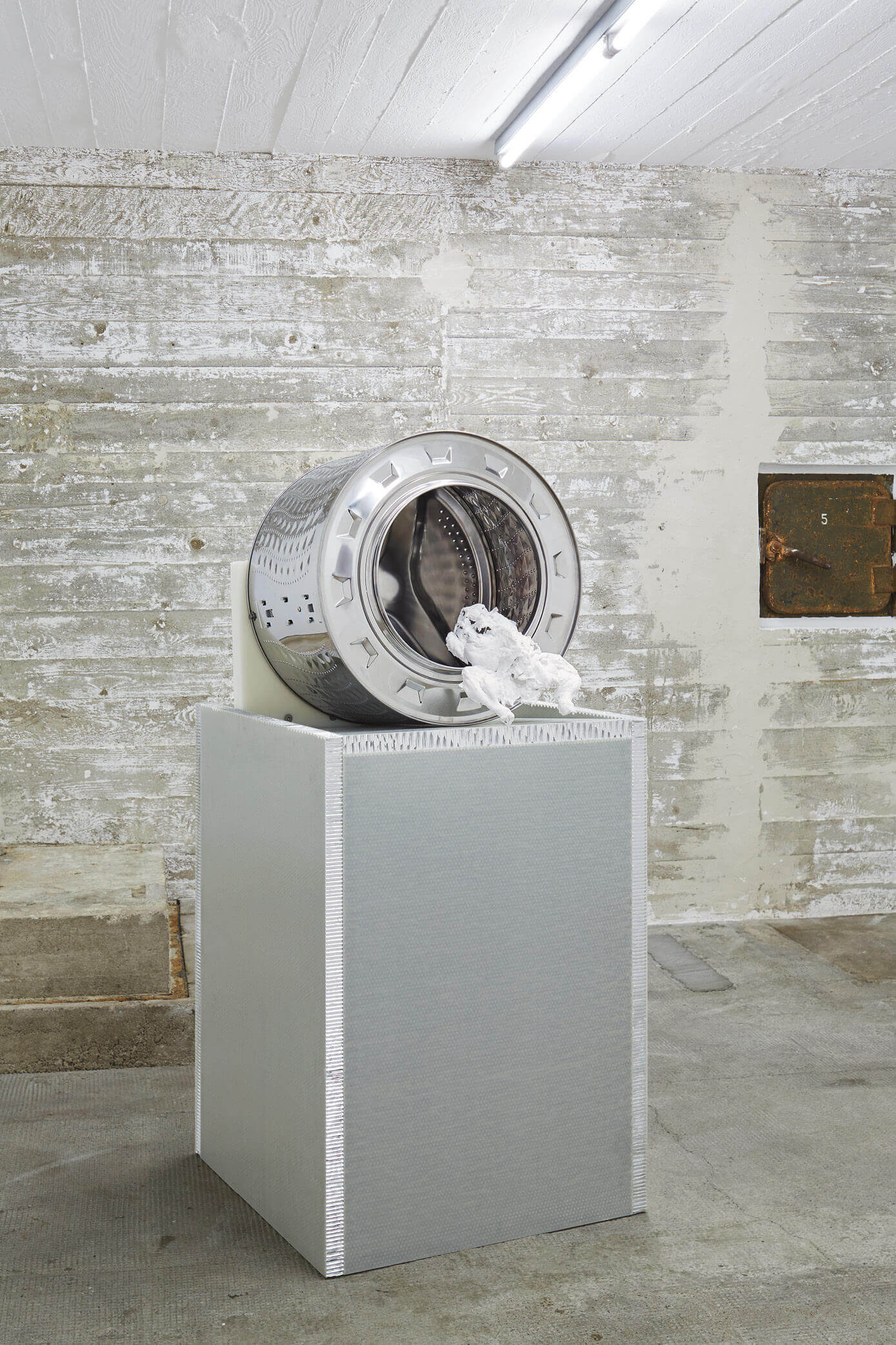 Skulptur mit Waschmaschinentrommel und weißem 3D-Objekt auf silbernem Sockel – Werk von Yngve Holen in der Boros Collection.